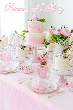 a table topped with pink and white cakes covered in frosted icing next to cups and saucers