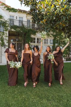 four bridesmaids in brown dresses holding bouquets and posing for the camera with their arms up