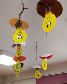 two yellow light bulbs with faces hanging from them, one has a hat on top