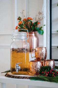 a glass jar filled with liquid sitting on top of a table next to copper cups