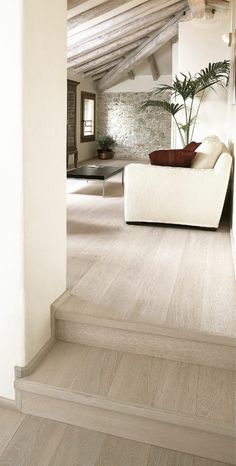 a white couch sitting on top of a wooden floor in a living room next to a window