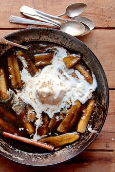 a bowl filled with food on top of a wooden table next to two spoons