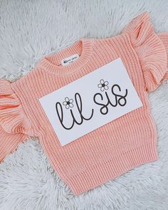 an orange sweater with the word lils on it sitting on a fluffy white surface