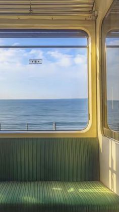 an empty bench sitting on the side of a train next to the ocean in front of a window