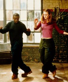 two people are dancing on the floor in an empty room with brick walls and large windows