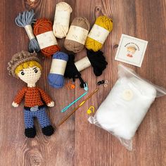 a knitted doll sitting on top of a wooden floor next to knitting supplies