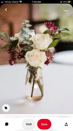 a vase filled with white flowers sitting on top of a table next to a cell phone