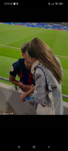 a man and woman kissing in front of a soccer field at the end of a game