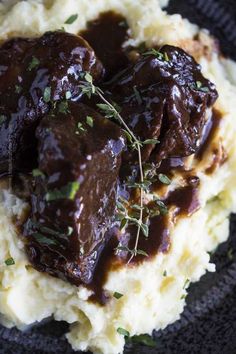 meat and gravy on mashed potatoes in a black plate with garnish