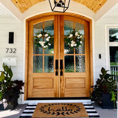 the front door is decorated with wreaths and potted plants, along with a welcome mat