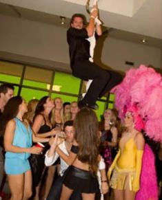 a man is standing on top of a woman in a pink feathered costume at a party