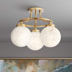 three globe lights hanging from a ceiling fixture in a room with a painting on the wall