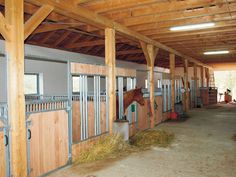 the inside of a stable with stalls and horses eating hay on the bales in front of them