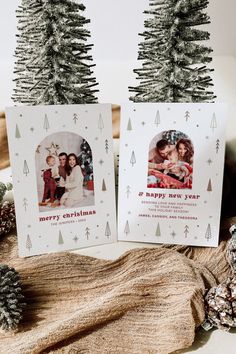 two christmas cards sitting on top of a table next to pine cones and fir trees