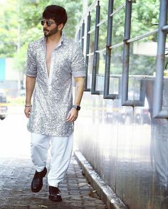 a man walking down the street wearing white pants and a shirt with silver sequins on it