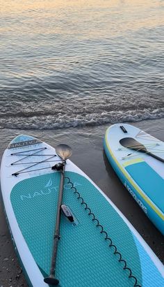 two surfboards sitting on top of a beach next to the ocean with paddles