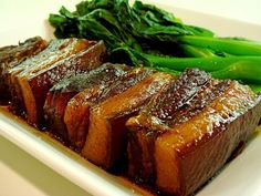 some meat and green vegetables on a white plate with brown sauce in front of it