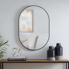 a mirror on the wall above a table with vases and a potted plant