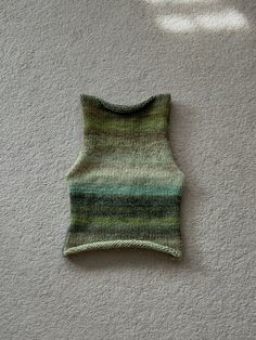 a green knitted sweater sitting on top of a white floor next to a wall