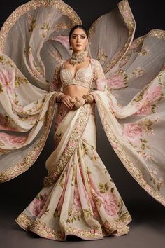 A stunning image of a Pakistani bride in an exquisite floral saree, with a delicate ivory base adorned with pastel pink and green embroidery. The saree is elegantly bordered with intricate gold zari work, adding a touch of opulence. The bride wears a low-cut blouse and is adorned with statement jewelry, including a magnificent necklace and earrings that enhance the grandeur of her bridal attire. The rich, layered drape of the saree flows effortlessly, creating a luxurious and modern bridal look that is truly captivating. Plus Size Indian Bride, Indian Bride In Saree, Sarees Photoshoot, Bengali Clothes, Bride In Saree, Sangeet Lehenga, Saree Borders, Saffron Spice, Cut Blouse