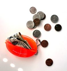 an orange container filled with money sitting on top of a white table next to coins