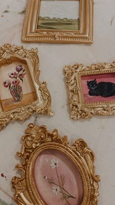 there are four framed pictures on the table with one black cat sitting in the middle