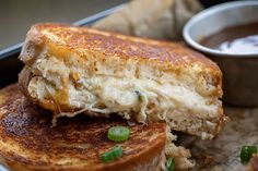 a close up of a sandwich on a plate with some sauce in the bowl behind it