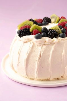 a white cake topped with fruit on top of a white plate next to a pink background