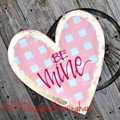 a heart shaped sign with the words be mine on it hanging from a wooden fence