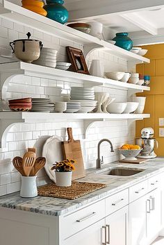 a kitchen with white cabinets and shelves filled with plates, bowls, knives and utensils