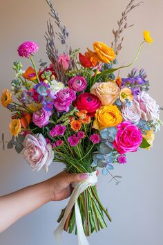 a person holding a bouquet of colorful flowers in their left hand and the other hand