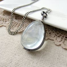 A teardrop glass locket sways gracefully from a sterling silver ball chain necklace.  The locket is encased in sterling silver and swivels from the bail , the contents can be seen from either side. The antique glass has a faint pale green cast, it's domed  to highlight the treasure beneath.  The pendant has a screw top closure, it opens by twisting the silver bead screw at the top. The locket and chain have been oxidized and buffed to highlight and add depth to the metal.Please note, the locket Silver Teardrop Locket Necklace, Silver Teardrop Locket Jewelry, Clear Locket Necklace, Push Gifts, Sterling Silver Locket, Glass Locket, Silver Locket, Ball Chain Necklace, Photo Locket