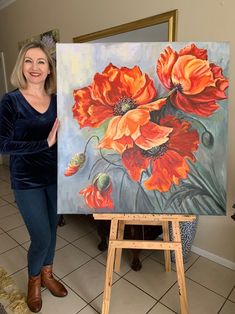 a woman standing next to an easel holding up a large painting on a canvas