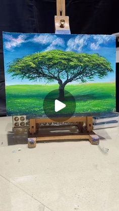 an easel with a painting on it that has a tree and blue sky in the background