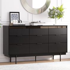 a black dresser sitting in front of a mirror on top of a wooden floor next to a plant