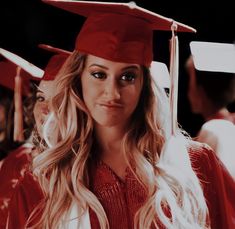 a woman wearing a red graduation cap and gown with long blonde hair in front of other graduates