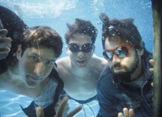 three men are underwater in the water with their hands up and one man is wearing sunglasses