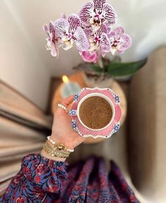 a woman holding a cup of coffee with orchids on the table in the background