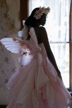 a woman in a dress with wings and flowers on her head is looking out the window