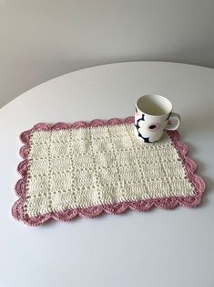 a crocheted placemat with a coffee cup on it sitting on a table