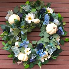 a wreath with white pumpkins, blue flowers and green leaves on a wooden surface