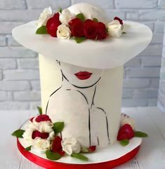 a white cake with red and white flowers on top, sitting on a table next to a brick wall