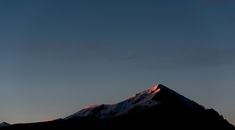 the sun is setting behind a mountain with snow on it's top and some clouds in the sky