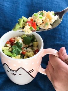 a person is holding a spoon over a cup with food in it on a blue cloth