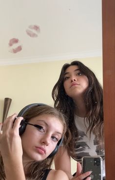 two girls are looking in the mirror and one is holding a cell phone to her ear