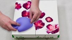 two hands are holding an object in front of a box with flowers painted on it