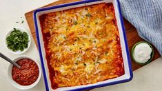 a casserole dish with cheese and sauce on a cutting board next to small bowls of condiments