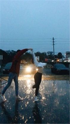 two people jumping in the air on a wet street at night with cars behind them