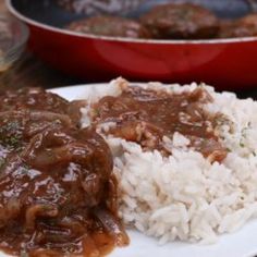 a white plate topped with rice and meat covered in gravy on top of a wooden table