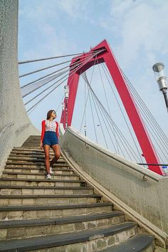 a woman is walking down some stairs in front of a red and white bridge over water